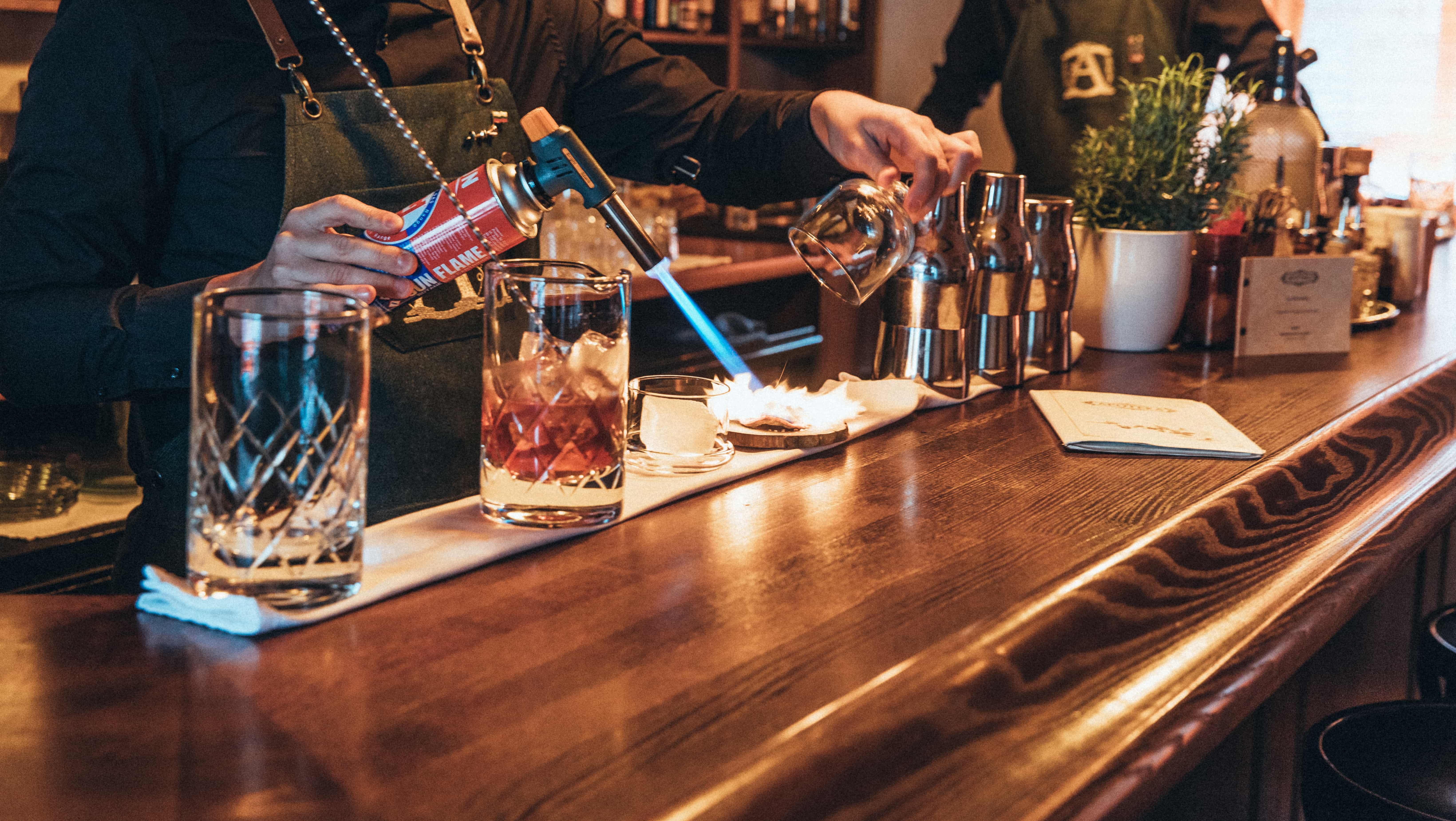 A display of the professionalism that is present for every cocktail made in Apoteka - the bartender's handling a torch in order to create an oak smoke infused cocktail.